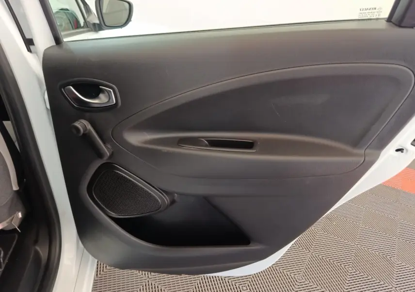 Vue intérieure de la porte arrière gauche noire de la Renault ZOE blanche Zen R135, avec poignée et haut-parleur intégrés.