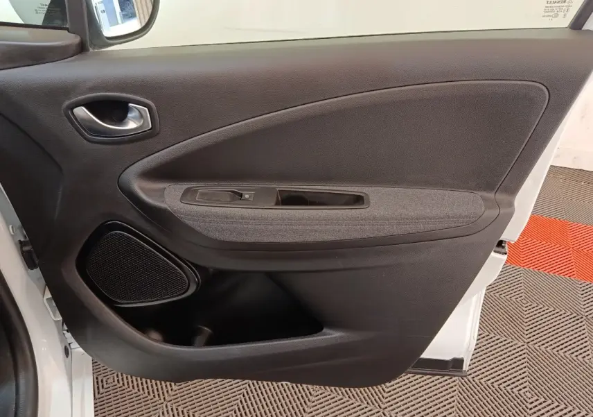 Vue intérieure de la porte avant gauche d'une Renault ZOE blanche, montrant la poignée, l'accoudoir et le haut-parleur intégré.