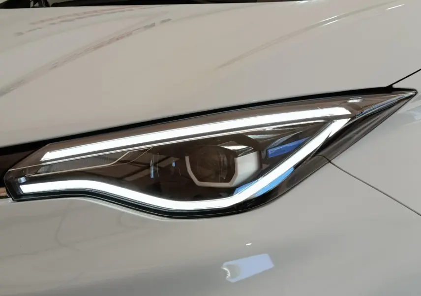 Gros plan sur le phare avant droit LED d'une Renault ZOE Zen R135 blanche, soulignant sa signature lumineuse moderne.