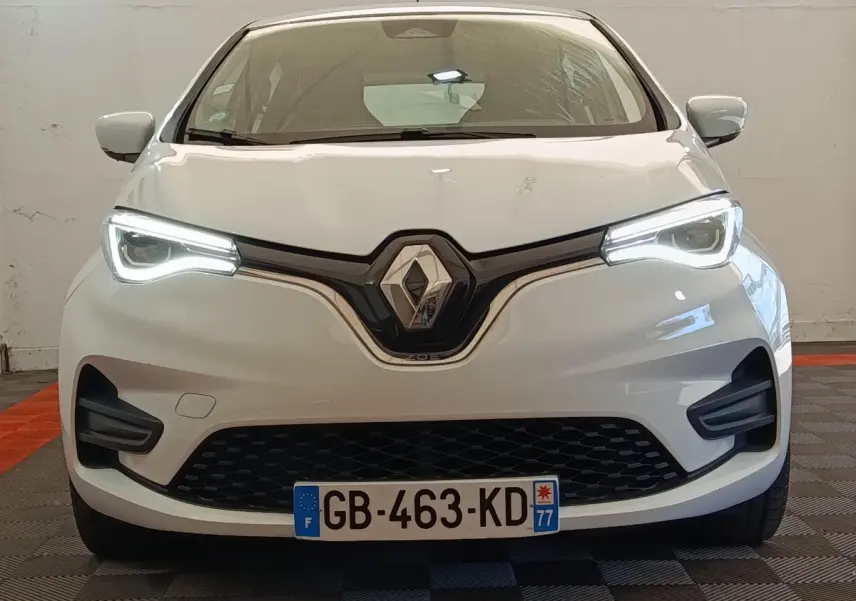 Vue avant d'une Renault ZOE Zen R135 blanche de 2021, avec phares LED allumés et calandre noire distinctive.