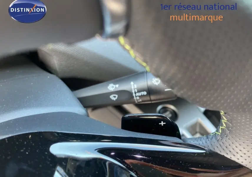 Gros plan sur la palette de changement de vitesse + du volant perforé avec surpiqûres jaunes d'une Peugeot 308 Hybrid blanche.