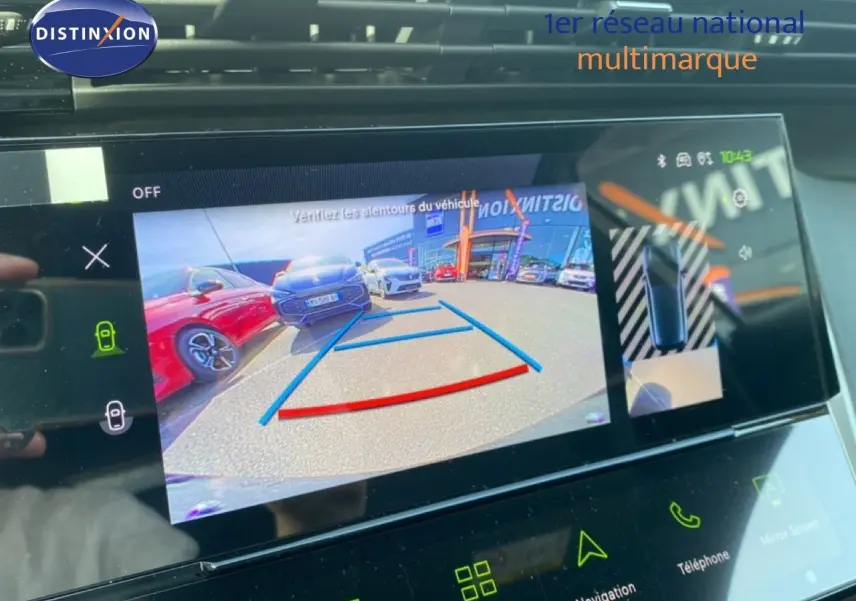 Écran tactile intérieur de Peugeot 308 Hybrid blanc montrant la caméra de recul avec vue arrière et voitures en stationnement.