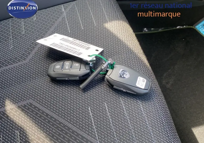Gros plan sur les clés de la Peugeot 308 Hybrid 145ch posées sur un siège tissu gris foncé à motifs blancs.