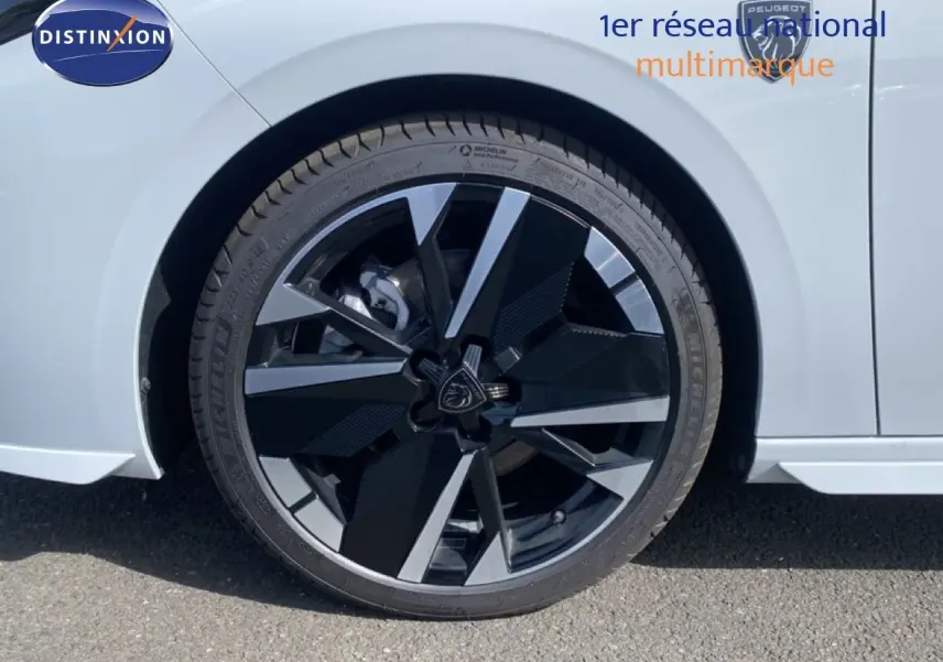 Gros plan sur la roue avant droite d'une Peugeot 308 Hybrid blanche, avec jante alliage noire et argentée au design moderne.