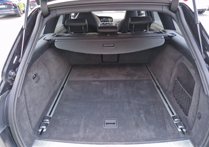 Coffre ouvert vu de l'arrière d'une Audi RS6 Avant noire de 2009, avec intérieur de coffre spacieux et tapis en tissu gris.