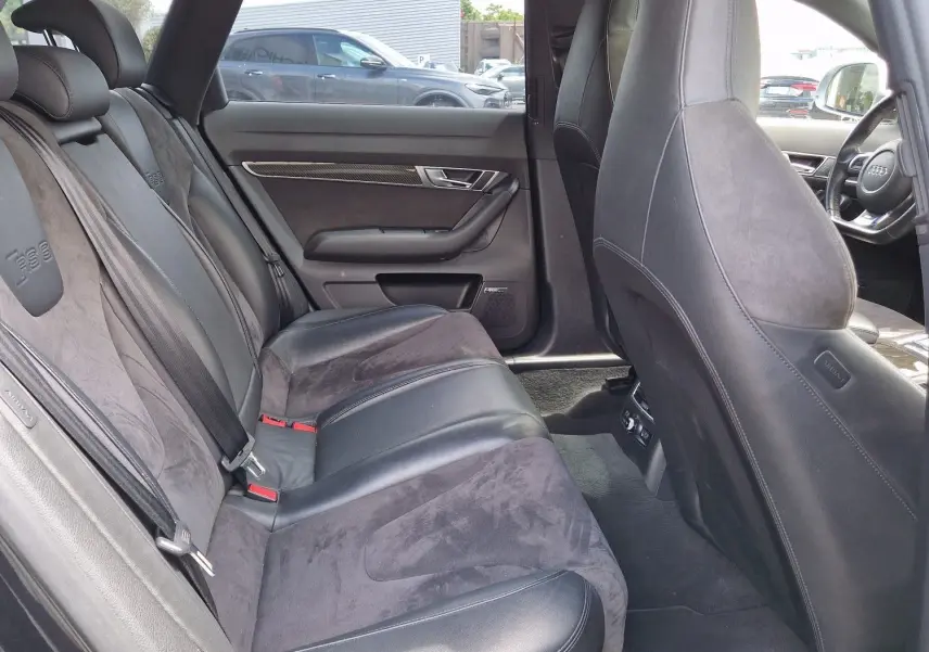 Vue intérieure côté arrière droit de l'Audi RS6 Avant noire de 2009, montrant les sièges en cuir et alcantara avec logo RS6 brodé.