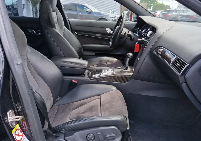Vue intérieure côté conducteur de l'Audi RS6 Avant noire de 2009, avec sièges sport en cuir et alcantara et console centrale en carbone.
