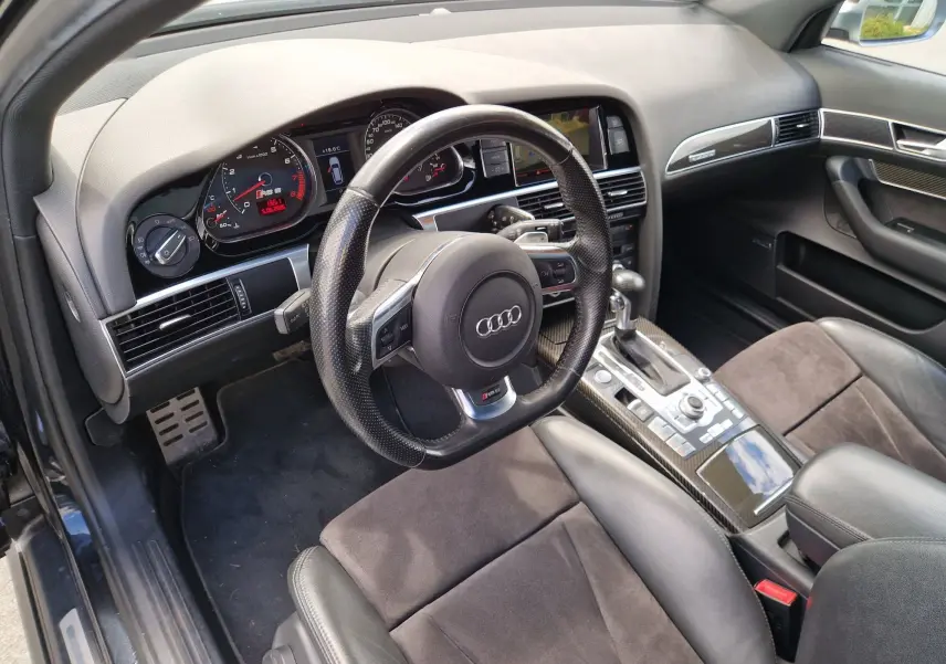 Vue intérieure côté conducteur de l'Audi RS6 Avant 2009 noire, avec volant sport, tableau de bord digital et console centrale carbone.