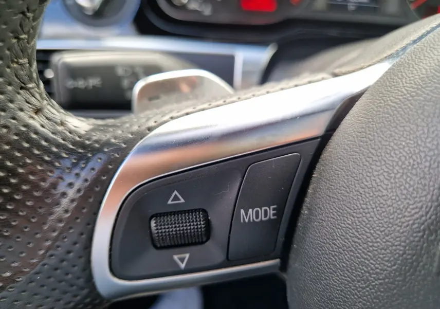 Gros plan sur les commandes en cuir perforé du volant noir de l'Audi RS6 Avant 2009, bouton mode et molette de réglage.