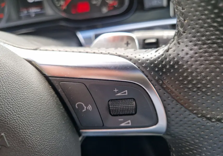 Gros plan sur les commandes de volume et de commande vocale au volant en cuir perforé de l'Audi RS6 Avant noir 2009.