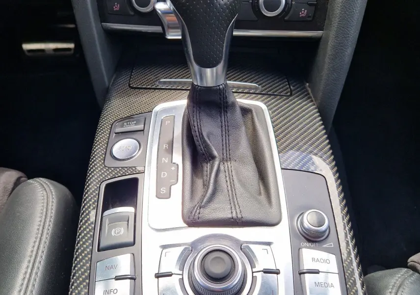 Vue rapprochée de la console centrale en carbone avec levier de vitesse automatique et commandes multimédia d'une Audi RS6 Avant noire.