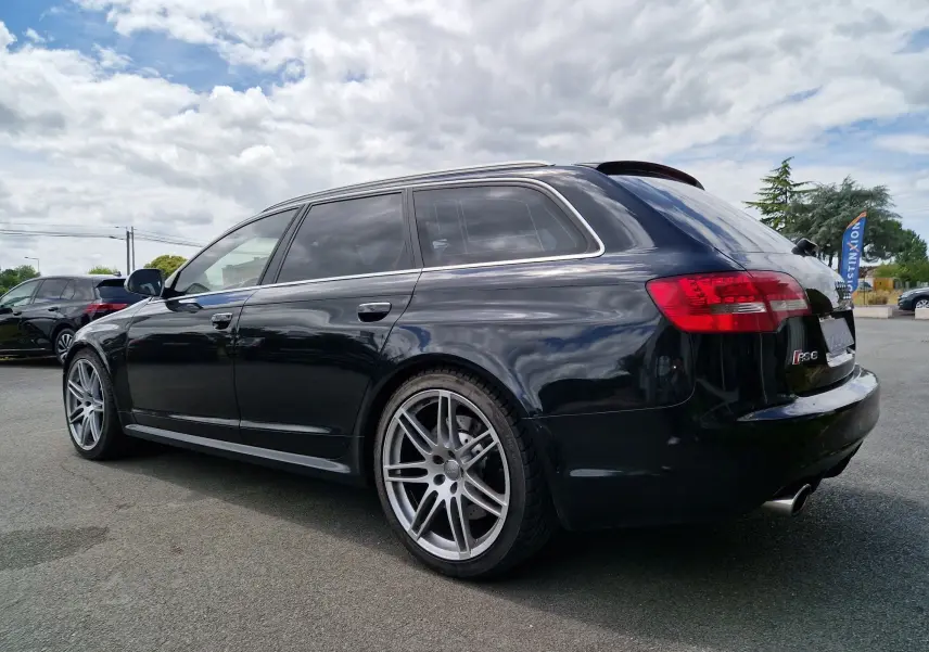 Audi RS6 Avant noire vue en 3/4 arrière côté droit, avec jantes alliage 20 pouces et feux arrière rouges.
