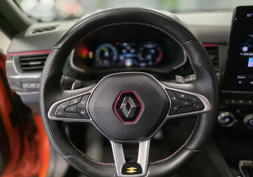 Volant sport en cuir perforé avec surpiqûres rouges et logo Renault au centre d'un Renault Arkana orange Valencia 2024.