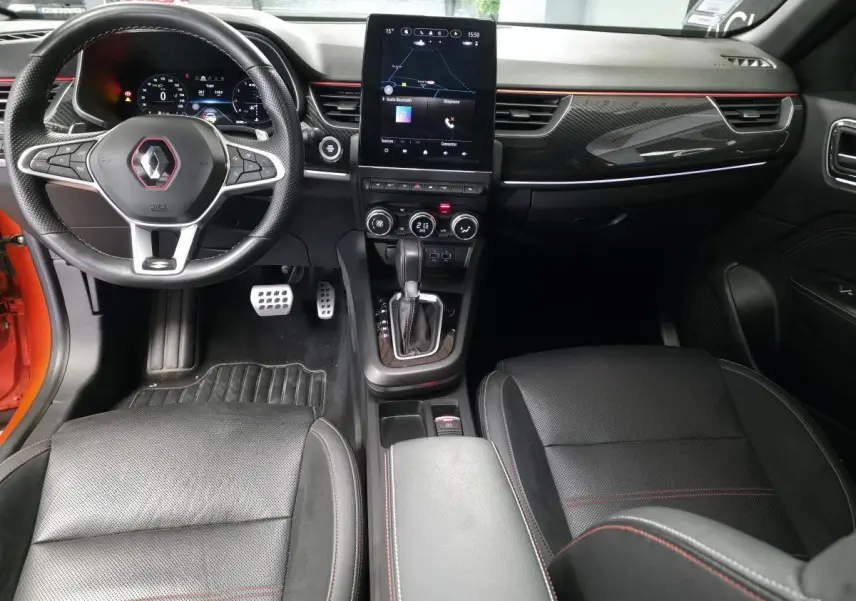 Intérieur avant du Renault Arkana 2024 R.S. Line avec volant sport, écran tactile vertical et surpiqûres rouges sur sièges noirs.