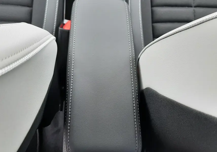 Vue plongeante sur l'accoudoir central noir entre les sièges gris clair et tissu noir du Citroën C3 Aircross 2025 hybride.