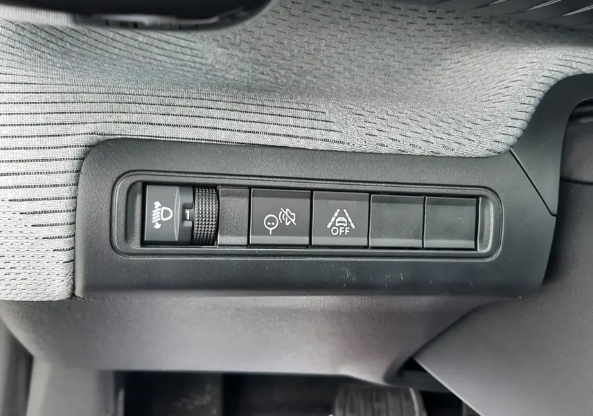 Gros plan sur les commandes d'assistance et réglage des phares dans l'habitacle gris clair du Citroën C3 Aircross hybride 2025.