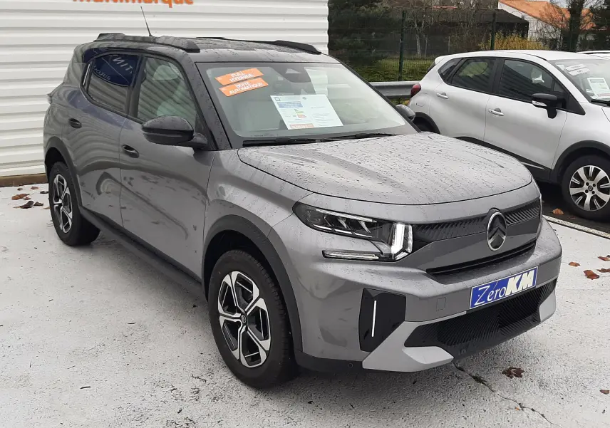 Citroën C3 Aircross hybride gris Mercury avec toit noir, vue 3/4 avant droit sous la pluie sur parking multimarque.
