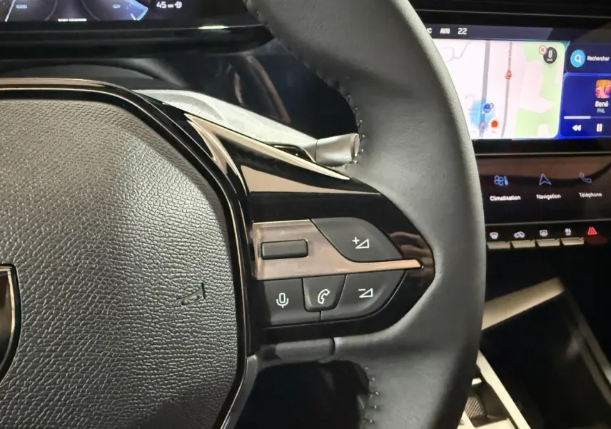 Gros plan sur le volant cuir à commandes multifonctions côté droit du Peugeot 308 rouge, avec écran tactile de navigation en arrière-plan.