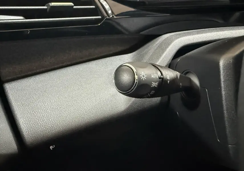 Gros plan sur la commande des phares à gauche du volant dans l’habitacle noir de la Peugeot 308 rouge 2025.