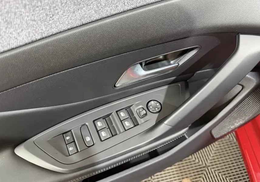 Vue rapprochée de la porte côté conducteur de la Peugeot 308 rouge, avec commandes électriques des vitres et rétroviseurs.