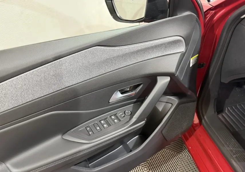 Vue intérieure côté gauche de la porte avant rouge de la Peugeot 308 BlueHDi 130 AUTO8 ALLURE avec commandes électriques.