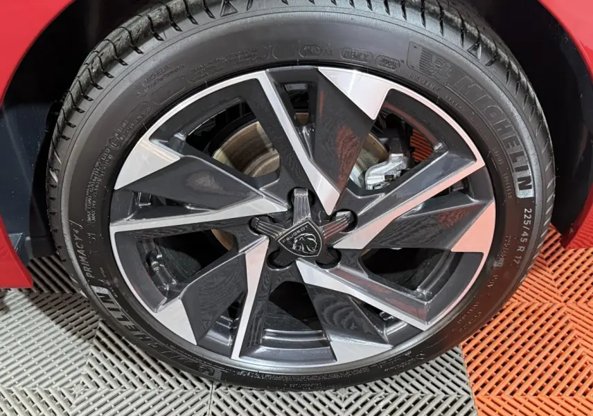 Gros plan sur la jante avant droite en alliage bicolore du Peugeot 308 rouge, avec logo lion central visible.