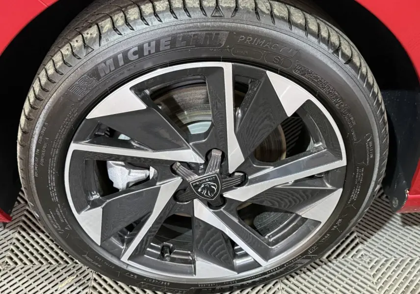 Gros plan sur la roue avant gauche d’une Peugeot 308 rouge 2025 avec jante alliage bicolore et pneu Michelin.
