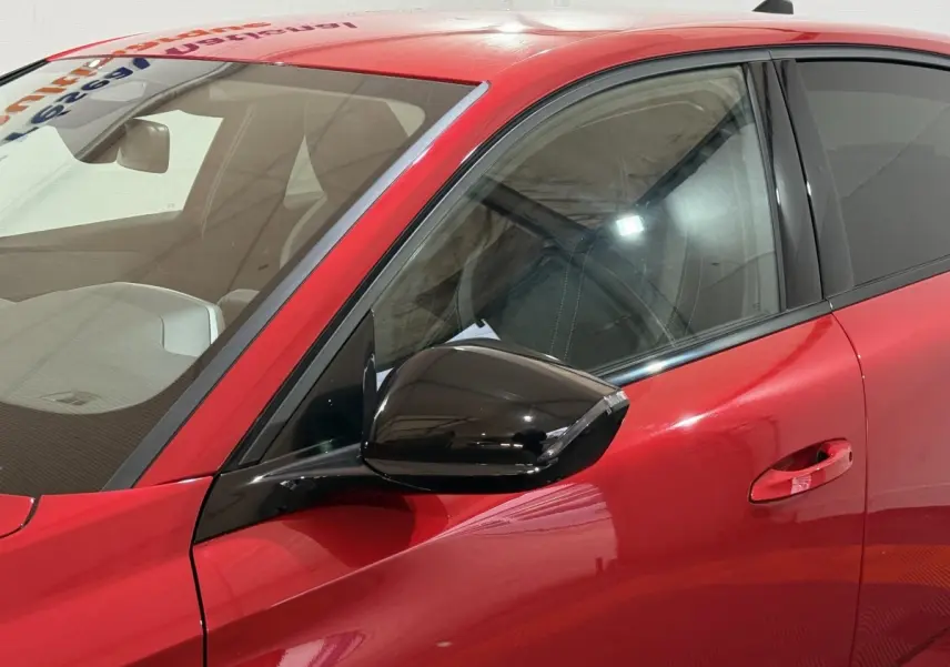 Vue rapprochée du côté avant gauche de la Peugeot 308 rouge avec rétroviseur noir brillant et poignée de porte intégrée.