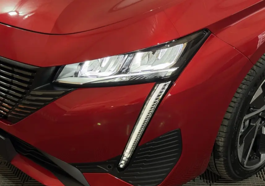 Gros plan sur l’avant droit rouge de la Peugeot 308 2025, mettant en valeur le phare LED et la calandre noire.