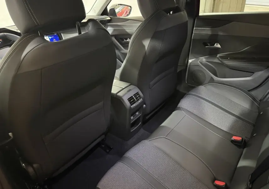Vue intérieure arrière montrant les sièges noirs et la console centrale d'une Peugeot 308 BlueHDi 130 AUTO8 Allure rouge.