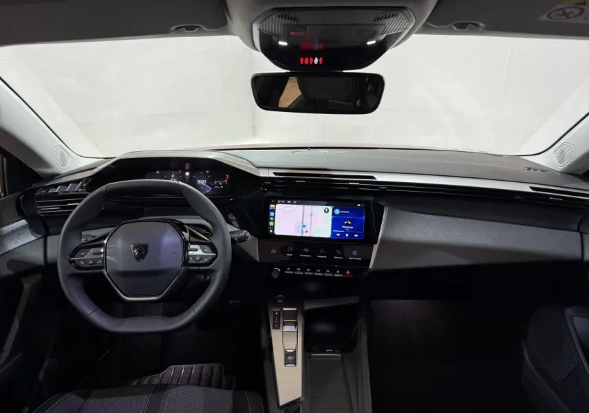 Vue intérieure avant du Peugeot 308 2025 avec tableau de bord noir, écran tactile central et volant cuir multifonctions.