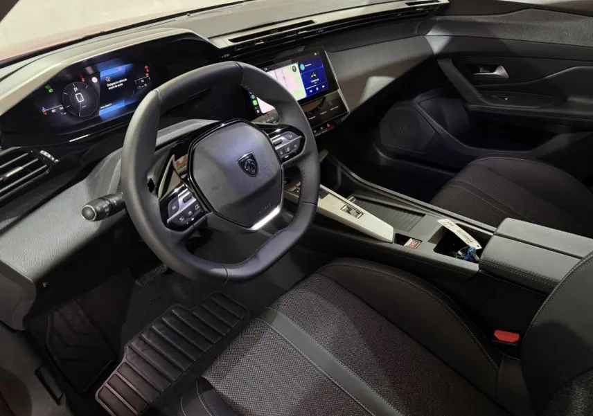 Intérieur de la Peugeot 308 2025 vue côté conducteur, volant cuir, tableau de bord numérique et écran tactile central.