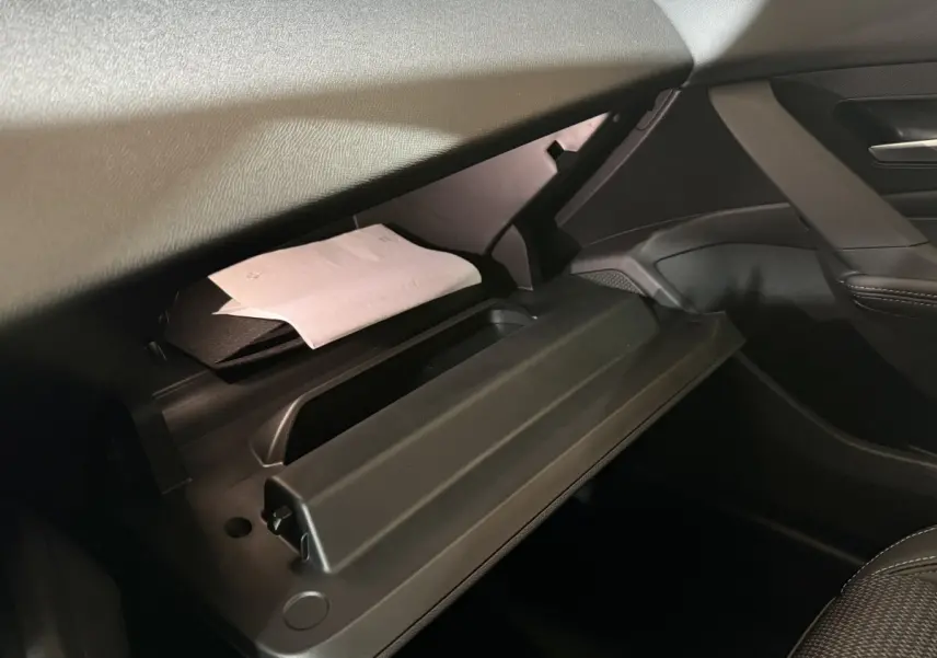 Intérieur de la Peugeot 308 2025, vue sur la boîte à gants ouverte côté passager avec documents visibles.