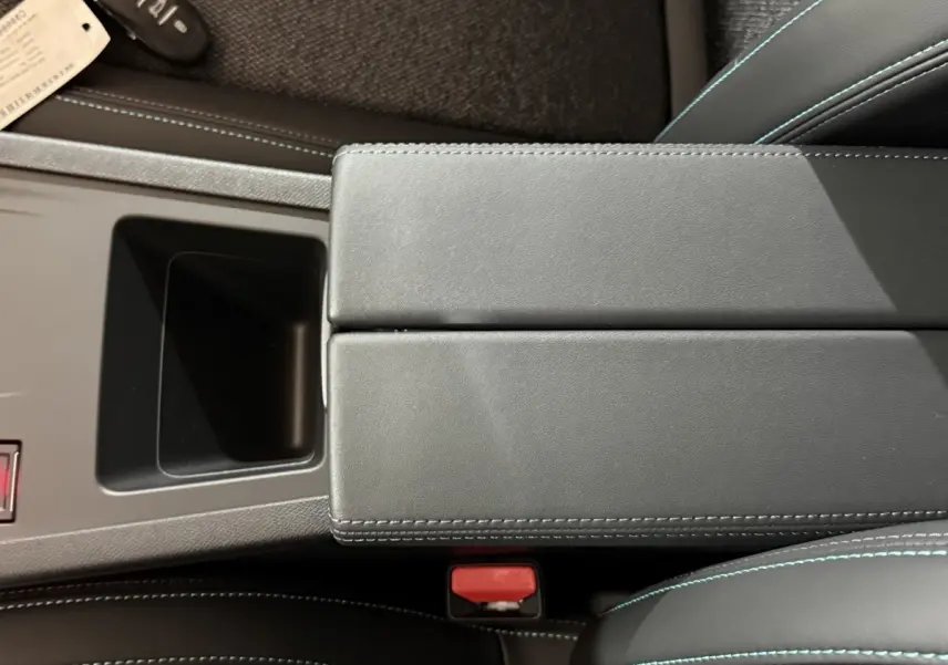 Vue rapprochée de l'accoudoir central noir et des sièges en cuir avec surpiqûres bleues dans une Peugeot 308 rouge.