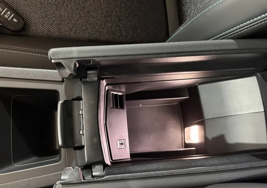 Vue intérieure en plongée du rangement central ouvert de la Peugeot 308 rouge, soulignant les finitions en cuir noir et coutures bleues.