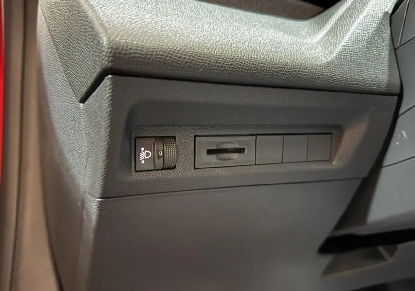 Détail intérieur côté gauche du tableau de bord noir de la Peugeot 308 rouge, avec commande réglage phares.