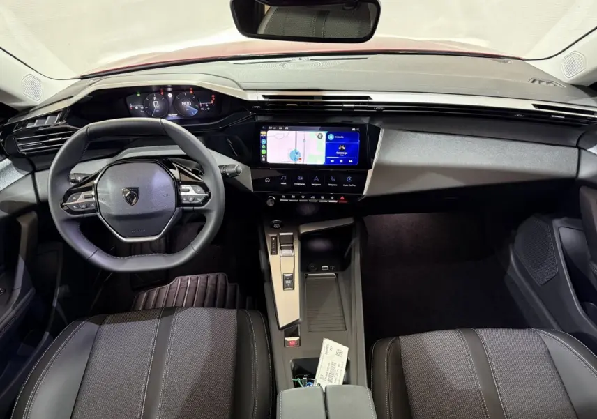 Vue intérieure avant de la Peugeot 308 2025, tableau de bord noir avec écran tactile central et volant multifonctions cuir.