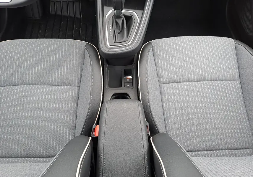 Vue intérieure centrée sur la console centrale et les sièges avant gris à surpiqûres blanches de la Renault Clio V hybride.