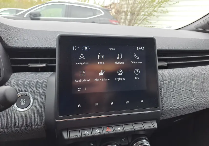 Vue intérieure centrée sur l’écran tactile du tableau de bord de la Renault Clio V hybride, avec bouton Start/Stop visible à gauche.
