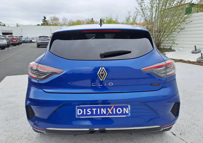 Vue arrière d'une Renault Clio V bleu iron metal avec feux LED et logo central, stationnée sur sol clair.