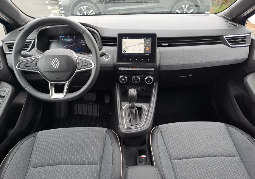 Vue intérieure avant de la Renault Clio V 1.6 E-TECH avec tableau de bord moderne, écran tactile central et sièges tissu gris.