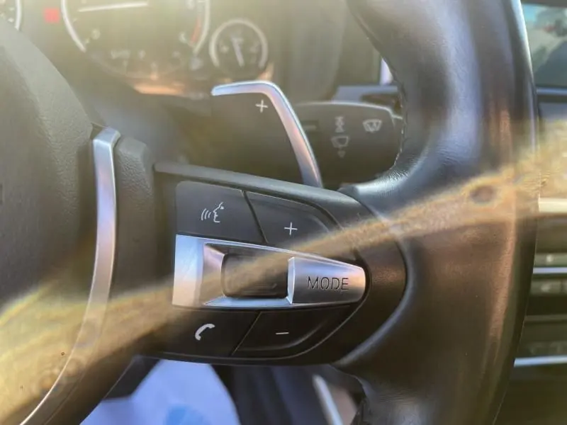 Détail du volant côté gauche d’un BMW X4 30DA X DRIVE noir métal de 2016, avec commandes vocales et mode audio.