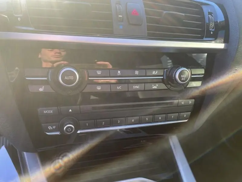 Vue rapprochée de la console centrale noire du BMW X4 30DA X Drive 2016, avec commandes climatisation et boutons M Sport.