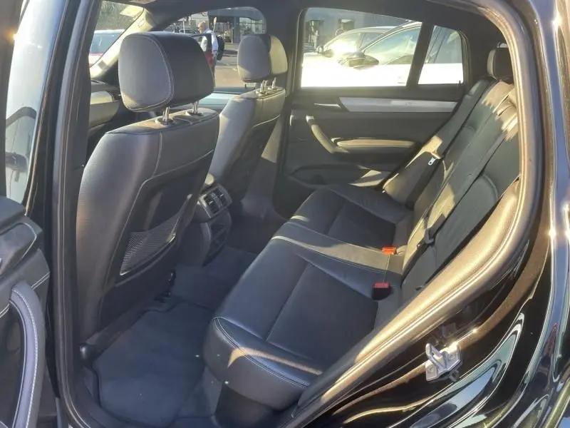 Vue intérieure arrière côté gauche du BMW X4 30DA X DRIVE noir métal, montrant les sièges en cuir et les détails de la porte ouverte.