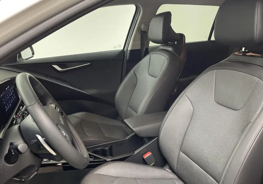 Intérieur du Kia Niro 2025 blanc, vue côté gauche sur les sièges avant en tissu gris et le volant multifonction.