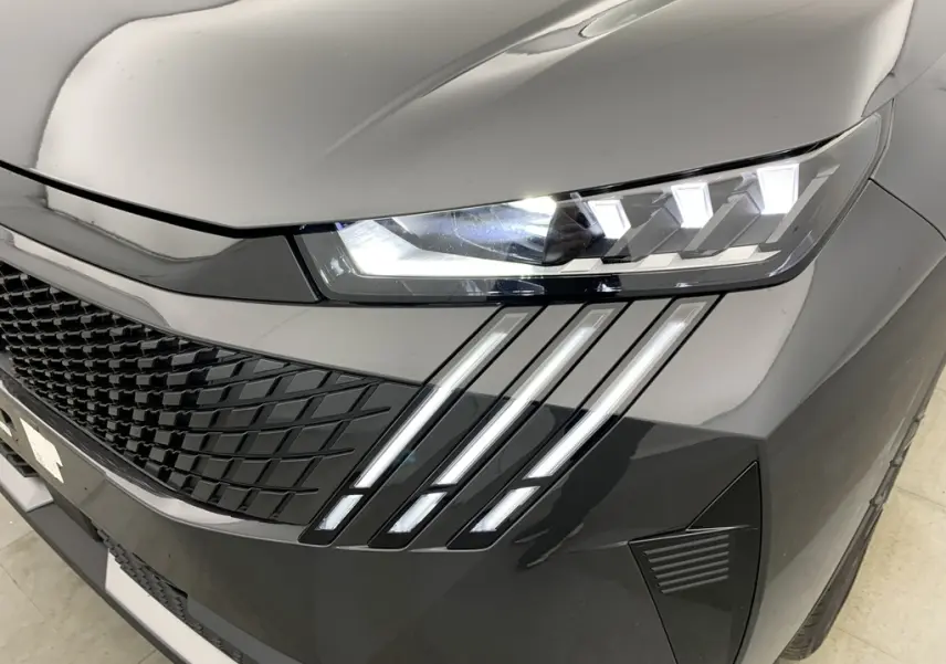 Gros plan sur le phare avant droit et la calandre noire laquée du Peugeot 3008 Hybrid gris Titane avec bandes LED distinctives.