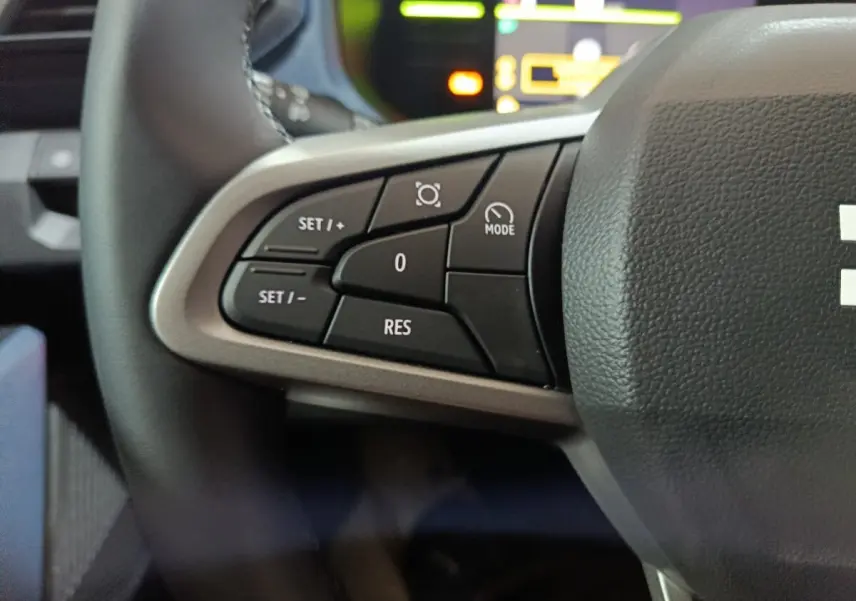 Gros plan sur les commandes de régulateur de vitesse au volant d’un Dacia Bigster gris foncé, intérieur moderne.