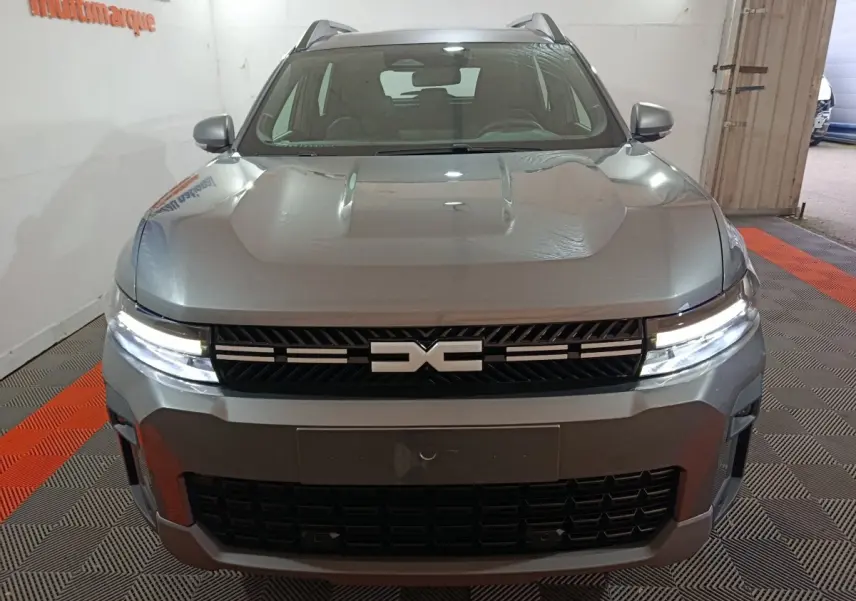 Vue avant du Dacia Bigster gris foncé avec calandre noire et feux LED allumés en intérieur.