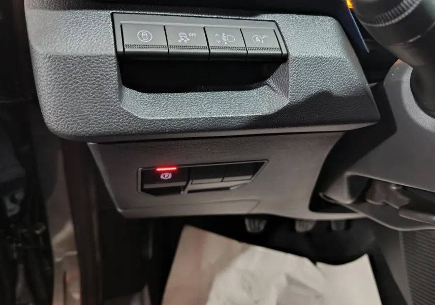 Détail des commandes sous le tableau de bord côté gauche du Dacia Bigster gris foncé, avec bouton frein à main électrique allumé.