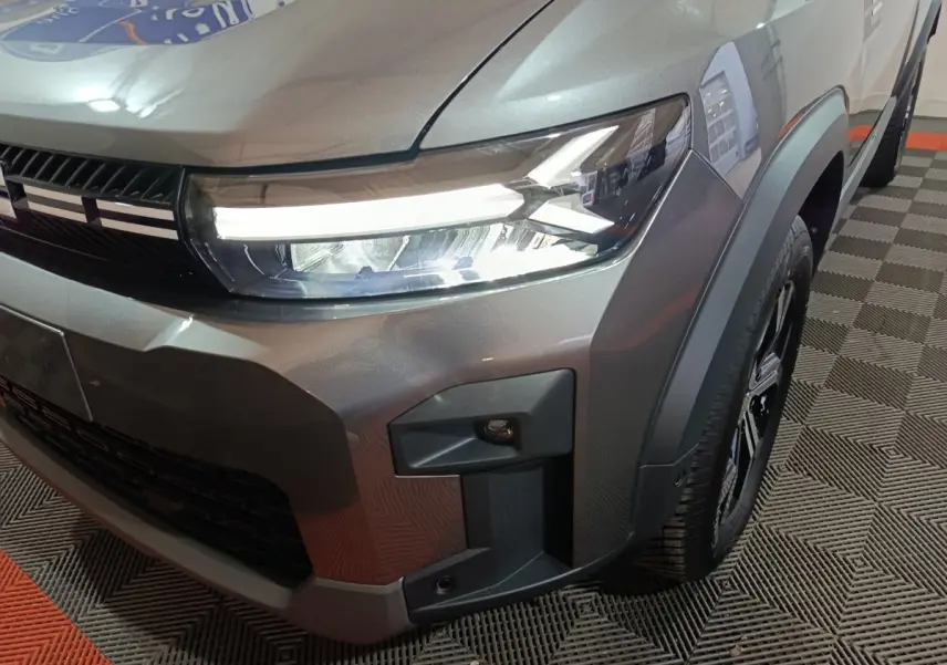 Gros plan sur l'avant droit du Dacia Bigster gris foncé, mettant en valeur le phare LED et la calandre noire.